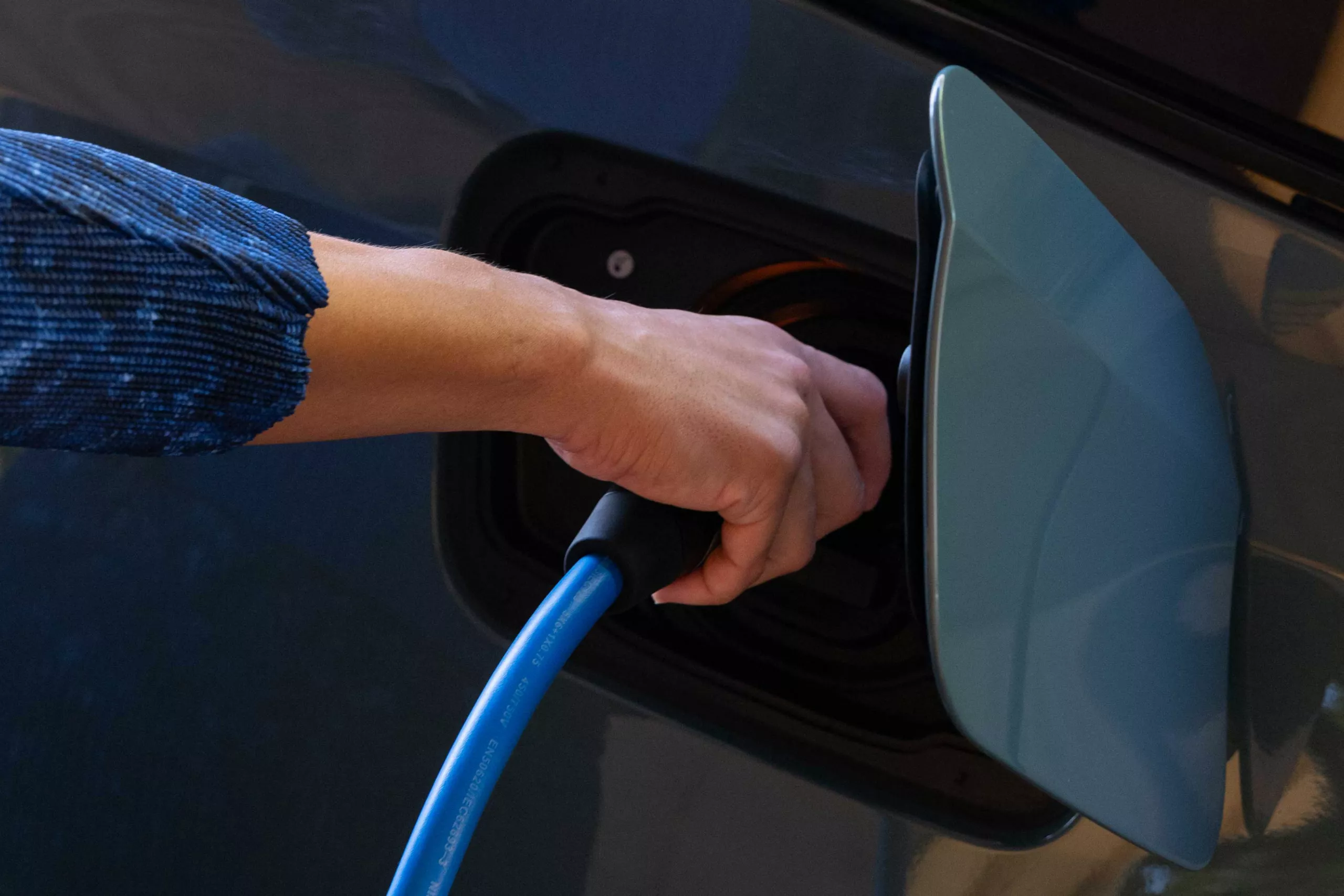  Eine Hand steckt ein blaues Ladekabel in den Ladeanschluss eines Elektroautos.