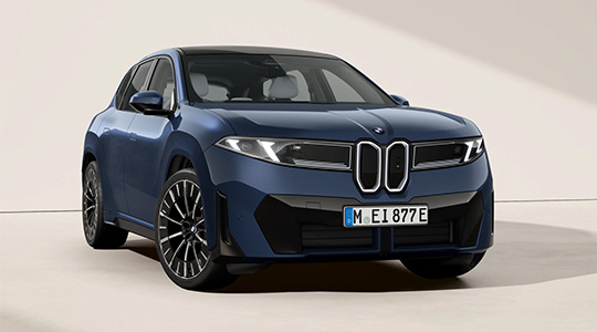 Frontansicht des vollelektrischen BMW iX3 (Modellgeneration Neue Klasse) in Dunkelblau im Studio, mit Fokus auf die markante Fahrzeugfront, die beleuchtete Doppelniere mit integrierten Scheinwerfern und große Alufelgen.