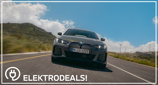 "Vorderansicht einer grauen BMW i4 Elektro-Limousine mit Kennzeichen 'MIA 122E', die auf einer Bergstraße an Windrädern vorbeifährt. Mit 'Elektrodeals!'-Logo."