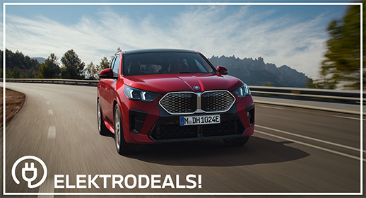 "Vorderansicht eines roten BMW iX2 Elektro-Crossovers mit Kennzeichen 'MDH 1024E', der auf einer Landstraße in Richtung Berge fährt. Mit 'Elektrodeals!'-Logo."