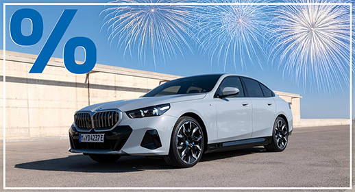 Diese Grafik zeigt eine vollelektrische BMW i5 Limousine in einem hellen Grauton, die auf einer weiten, asphaltierten Fläche vor einer schlichten Betonmauer parkt. Das Auto ist in einer eleganten Dreiviertelansicht von vorne dargestellt, wobei die modernen Felgen und die fließende Form der Karosserie besonders gut zur Geltung kommen. Der Hintergrund ist minimalistisch gehalten und zeigt einen klaren, strahlend blauen Himmel.  Über dem Fahrzeug erstrecken sich vier große, filigrane Feuerwerke in Weiß- und Blautönen, die dem sauberen Design eine festliche Note verleihen. Wie gewohnt wird die Grafik durch das markante blaue Prozentzeichen oben links und den umlaufenden weißen Rahmen als Teil der Aktionsserie zum Jahresstart gekennzeichnet.