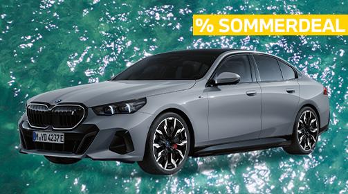 Ein moderner, silbergrauer BMW i5 eDrive40 Limousine steht auf einem türkisfarbenen Wasserhintergrund. Das Fahrzeug ist leicht von vorne links abgebildet, wodurch der markante schwarze Kühlergrill, die LED-Scheinwerfer und die linke Fahrzeugseite mit den auffälligen schwarzen Felgen gut sichtbar sind. Oben rechts im Bild befindet sich ein gelbes Banner mit der Aufschrift „% SOMMERDEAL“ in Großbuchstaben. Das Fahrzeug wirkt dynamisch und stromlinienförmig