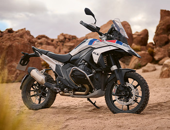 Das Bild zeigt eine moderne Reiseenduro, genauer gesagt eine BMW R 1300 GS in der sportlichen Trophy-Variante, die auf unbefestigtem Wüstenboden abgestellt ist.
